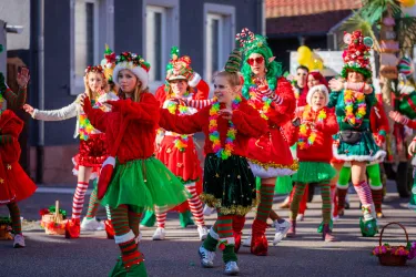 Eine fröhliche Parade mit verkleideten Teilnehmern in bunten, festlichen Outfits. Die Menschen tragen Weihnachtsdekorationen und tanzen in einer lebhaften Atmosphäre.