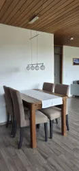 Ein moderner Essbereich mit einem Holztisch und vier beigen Stühlen. Die Wände sind schlicht und ein Holzdeckenverkleidung sorgt für eine warme Atmosphäre.
