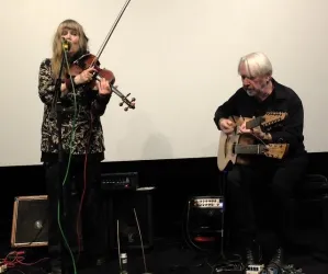Ein Musiker-Duo tritt auf. Die Frau spielt Geige und singt, während der Mann auf einer Gitarre spielt.
