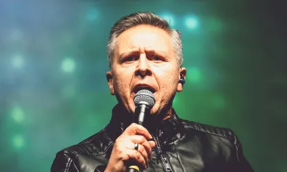 Ein Sänger mit Mikrofon hält eine leidenschaftliche Performance. Er trägt eine schwarze Lederjacke und hat einen intensiven Blick.