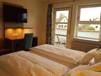 Ein gemütliches Hotelzimmer mit zwei Einzelbetten und einem Schreibtisch. Der Raum hat große Fenster mit Blick auf die Außenansicht und bietet natürliches Licht.