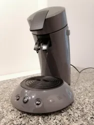 Ein moderner Wasserkocher in grauem Design steht auf einer hellen Granitoberfläche. Der Wasserkocher hat eine schlichte Form und befindet sich neben einer runden Basis mit Bedientasten.