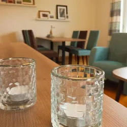 Ein gemütlicher Wohnraum mit einem Holztisch und bunten Stühlen. Auf dem Tisch stehen zwei Glaslaternen.