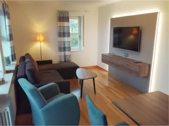 Ein modernes Wohnzimmer mit einem großen Sofa und einem Fernseher an der Wand. Ein eleganter Tisch und ein Stuhl vervollständigen die gemütliche Atmosphäre.