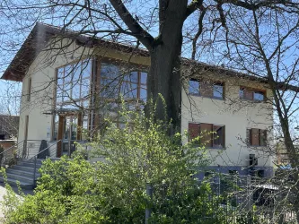 Ein modernes Haus - Forstamt - mit großen Fenstern und einem begrünten Außenbereich. Bäume und Pflanzen umgeben die Gebäude.