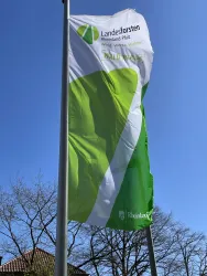 Eine große Fahne mit grünen und weißen Farben weht im Wind. Auf der Fahne steht "Landesforsten Rheinland-Pfalz".