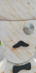 Eine Skulptur mit einem lächelnden Gesicht und einem Schnurrbart. Die Statue besteht aus hellem Stein und hat metallische Elemente.