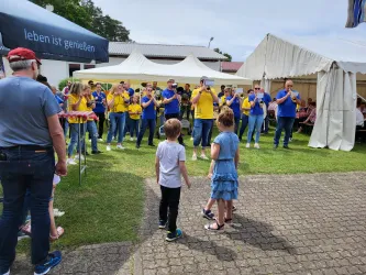 Eine Gruppe von Menschen in bunten Shirts spielt Musik auf einer Wiese. Im Vordergrund stehen zwei Kinder, die zuschauen.