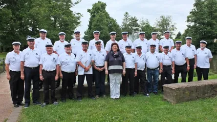 Eine Gruppe von Männern in weißen Hemden und Hüten steht auf einer Wiese. In der Mitte steht eine Frau in einem schwarzen Oberteil.