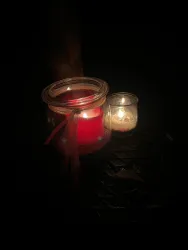 Eine rote Kerze in einem Glas und eine kleine weiße Kerze leuchten im Dunkeln. Die Atmosphäre ist gemütlich und entspannend.
