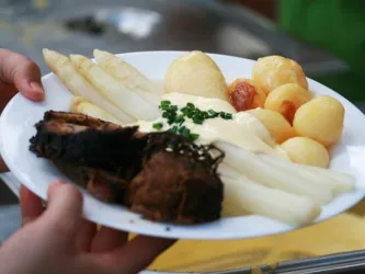 Ein Teller mit gekochtem Spargel, Kartoffeln und einem Stück Fleisch. Das Gericht ist mit Sauce und frischem Schnittlauch garniert.