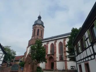 Eine beeindruckende Kirche mit einem hohen Turm und roten Ziegelsteinen. Umgeben von charmanten, historischen Gebäuden und Bäumen.