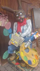 Eine bunte Statue eines Malerhasen mit einem Pinsel und einer Farbpalette. Der Hase trägt eine karierte Bluse und eine rote Schürze.