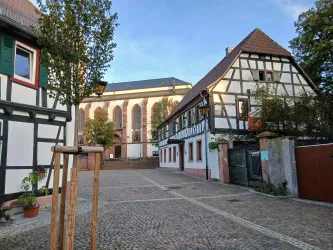Ein malerischer Platz mit historischen Fachwerkhäusern und einem Blick auf eine Kirche im Hintergrund. Die Atmosphäre ist ruhig und einladend.