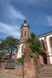 Eine alte Kirche mit einem hohen Turm und einer schönen Fassade. Im Vordergrund steht eine Statue, umgeben von Bäumen.