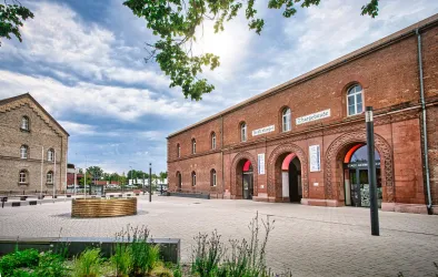 Ein schöner Platz mit historischen Backsteinbauten und einer modernen Brunneninstallation. Der Himmel ist bewölkt, und die Umgebung wirkt einladend.