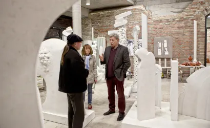 Eine Kunstgalerie mit modernen Skulpturen aus weißem Material. Drei Personen stehen im Gespräch zwischen den Exponaten.