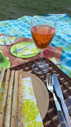 Ein schönes Picknick mit einer Gläsern Roséwein und knusprigen Stangenbrot. Die bunten Teller und das Dekor schaffen eine einladende Atmosphäre.