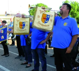 Eine Gruppe von Musikern in blauen T-Shirts hält Fahnen mit dem Wappen von Sonderheim. Sie stehen draußen bei einer Veranstaltung.