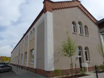 Ein modernes Gebäude mit einer schlichten, hellen Fassade. Es ist umgeben von neuem Grün und hat große Fenster.