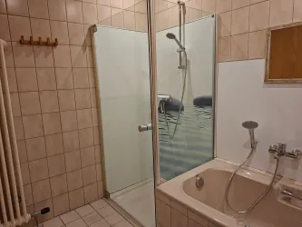 Ein Badezimmer mit einer Dusche und einer Badewanne. Die Wände sind gefliest und der Boden ist mit weißen Fliesen bedeckt.
