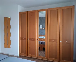 Ein Schlafzimmer mit einem großen, hellen Holzkleiderschrank und einem dekorativen Spiegel an der Wand. Der Raum hat eine ruhige Atmosphäre mit einem neutralen Farbschema.