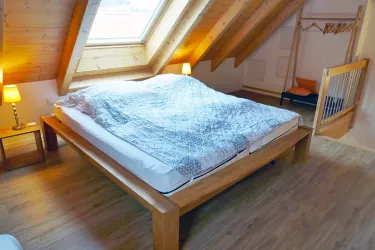 Ein gemütliches Schlafzimmer mit einem großen Holzbett und einem Dachfenster. Die warmen Holztöne schaffen eine einladende Atmosphäre.