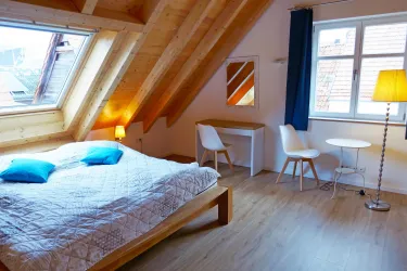 Ein gemütliches Schlafzimmer mit Holzdecken und hellen Wänden. Das Zimmer ist mit einem Doppelbett, einem Schreibtisch und einem kleinen Tisch ausgestattet.