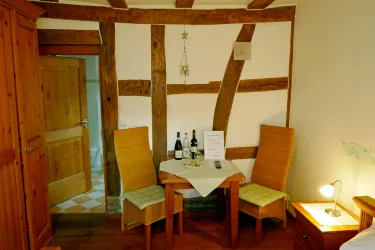 Ein gemütlicher Raum mit Holzwänden und einem kleinen Tisch. Zwei Stühle stehen um den Tisch, auf dem Flaschen Wein und ein Informationsblatt liegen.