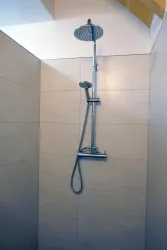 Eine moderne Dusche mit einem großen Kopfbrause und Handbrause. Die Wände sind hell gefliest und der Raum wirkt freundlich und einladend.