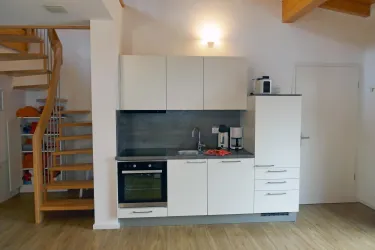 Eine moderne Küche mit weißen Schränken und einem Herd. Im Hintergrund sieht man eine Treppe und einen Aufbewahrungsschrank.