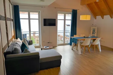 Ein modernes Wohnzimmer mit einem großen Sofa und einem Esstisch. Große Fenster lassen viel Licht herein und bieten einen Blick nach draußen.