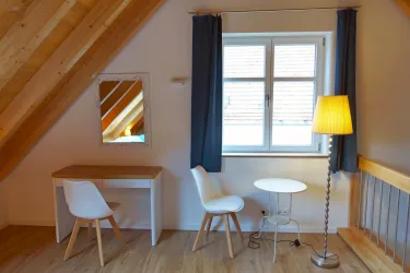 Ein gemütliches Zimmer mit zwei Stühlen und einem Tisch. Das große Fenster sorgt für viel Tageslicht.