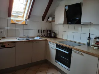 Eine moderne Küche mit Holzarbeitsfläche und weißen Schränken. Es gibt einen Herd, einen Kühlschrank und verschiedene Küchengeräte.