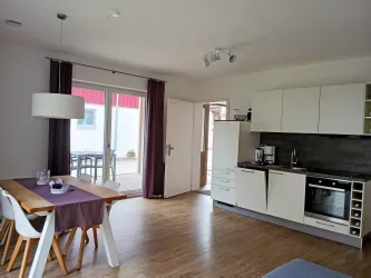 Eine moderne Küche mit einem Esstisch und Stühlen. Große Fenster sorgen für viel Tageslicht und Blick nach draußen.