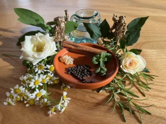 Ein dekoratives Arrangement mit frischen Kräutern, Gewürzen und Blumen. In der Mitte befindet sich eine Schale mit verschiedenen Zutaten, umgeben von Pflanzen und kleinen Figuren.