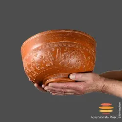 Eine handgefertigte Terrakottaschüssel mit detaillierten Reliefs. Sie wird von zwei Händen gehalten und hat eine warme, orangebraune Farbe.