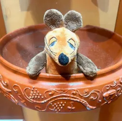 Eine niedliche Stoffmaus sitzt in einem Blumentopf. Die Maus hat große Ohren und einen freundlichen Gesichtsausdruck.