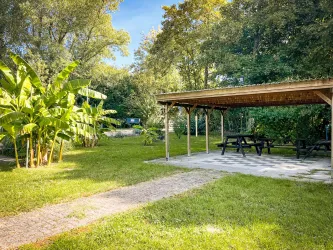 Ein ruhiger Garten mit einer überdachten Sitzgelegenheit und viel Grün. In der Nähe stehen große Pflanzen und Bäume.