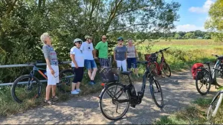 Eine Gruppe von Menschen steht mit Fahrrädern auf einem Radweg. Sie genießen die Natur in einer ländlichen Umgebung.