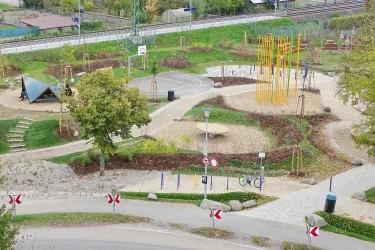 Ein Spielplatz mit verschiedenen Spielgeräten und einem Basketballplatz. Die Umgebung ist grün und einladend gestaltet.