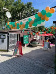 Ein einladender Eingang mit bunten Luftballons in Grün, Orange und Gelb. Im Hintergrund sind Schilder und Sitzgelegenheiten zu sehen, die eine fröhliche Atmosphäre schaffen.