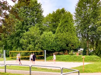 Ein Volleyballfeld in einer grünen Umgebung. Einige Personen spielen Volleyball unter einem klaren Himmel.