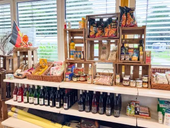 Ein Verkaufsregal mit verschiedenen Lebensmitteln und Getränken. Auf der obersten Ebene sind Snacks und Saucen in Holzkisten angeordnet.