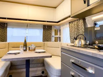 Ein moderner Wohnmobil-Innenraum mit einer gemütlichen Sitzecke und einer kleinen Küche. Der Tisch ist gedeckt und eine Flasche Wein steht bereit.