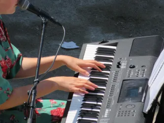 Eine Person spielt Klavier und singt gleichzeitig. Die Hände bewegen sich über die Tasten eines elektronischen Keyboards.