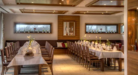 Ein eleganter Veranstaltungsraum mit langen Tischen und Holzstühlen. Die Atmosphäre ist warm und einladend, perfekt für Feiern oder Meetings.