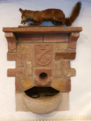 Ein alter Stein mit einer Tierpräparation eines Fuchses oben drauf. Die Jahreszahl 1428 ist in den Stein eingraviert.