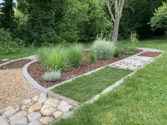 Ein schön angelegter Gartenweg mit verschiedenen Pflanzen und Kieselsteinen. Die grüne Umgebung sorgt für eine ruhige und einladende Atmosphäre.