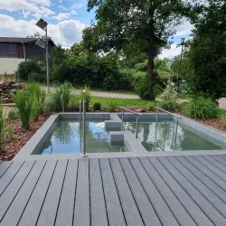Ein modernes Wasserbecken in einem hübsch gestalteten Garten. Umgeben von Pflanzen und einem Holzterrassenboden.